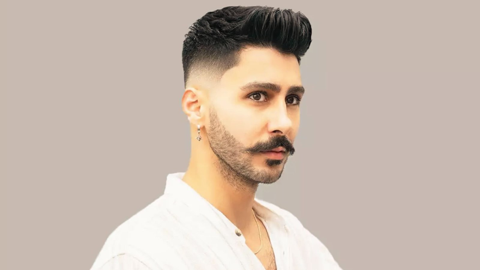 A man with a moustache wearing a white shirt, showcasing a blowout disconnected undercut fade hairstyle.