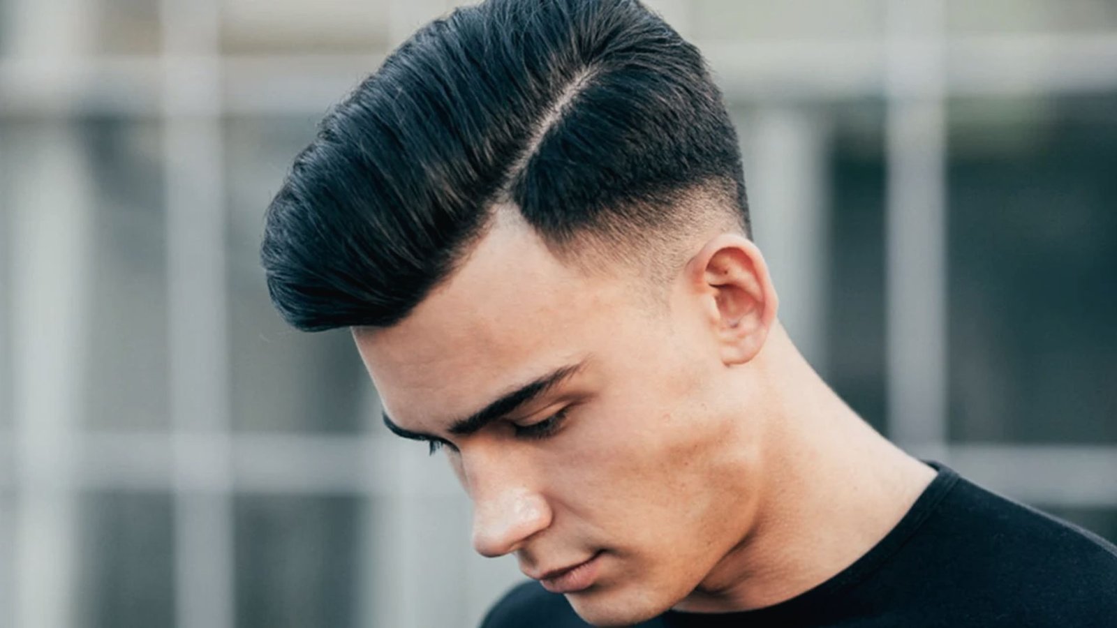 A man in a black shirt with a slicked-back disconnected undercut fade hairstyle and a short haircut.