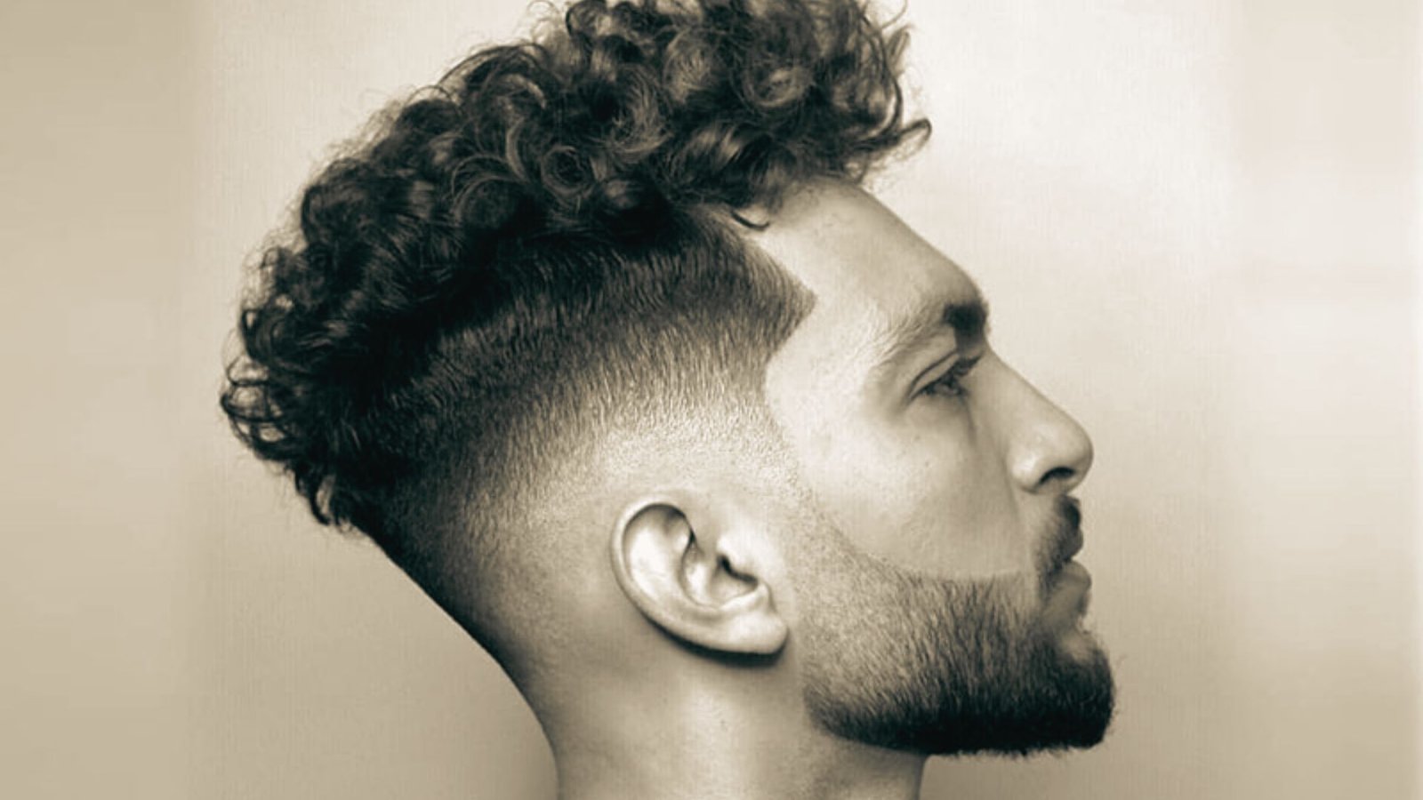 A man with curly hair and beard, featuring a natural curl disconnected undercut fade hairstyle.