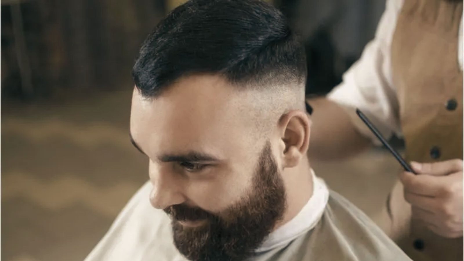 A man with a beard receives a haircut, showcasing a bedhead disconnected undercut fade style.