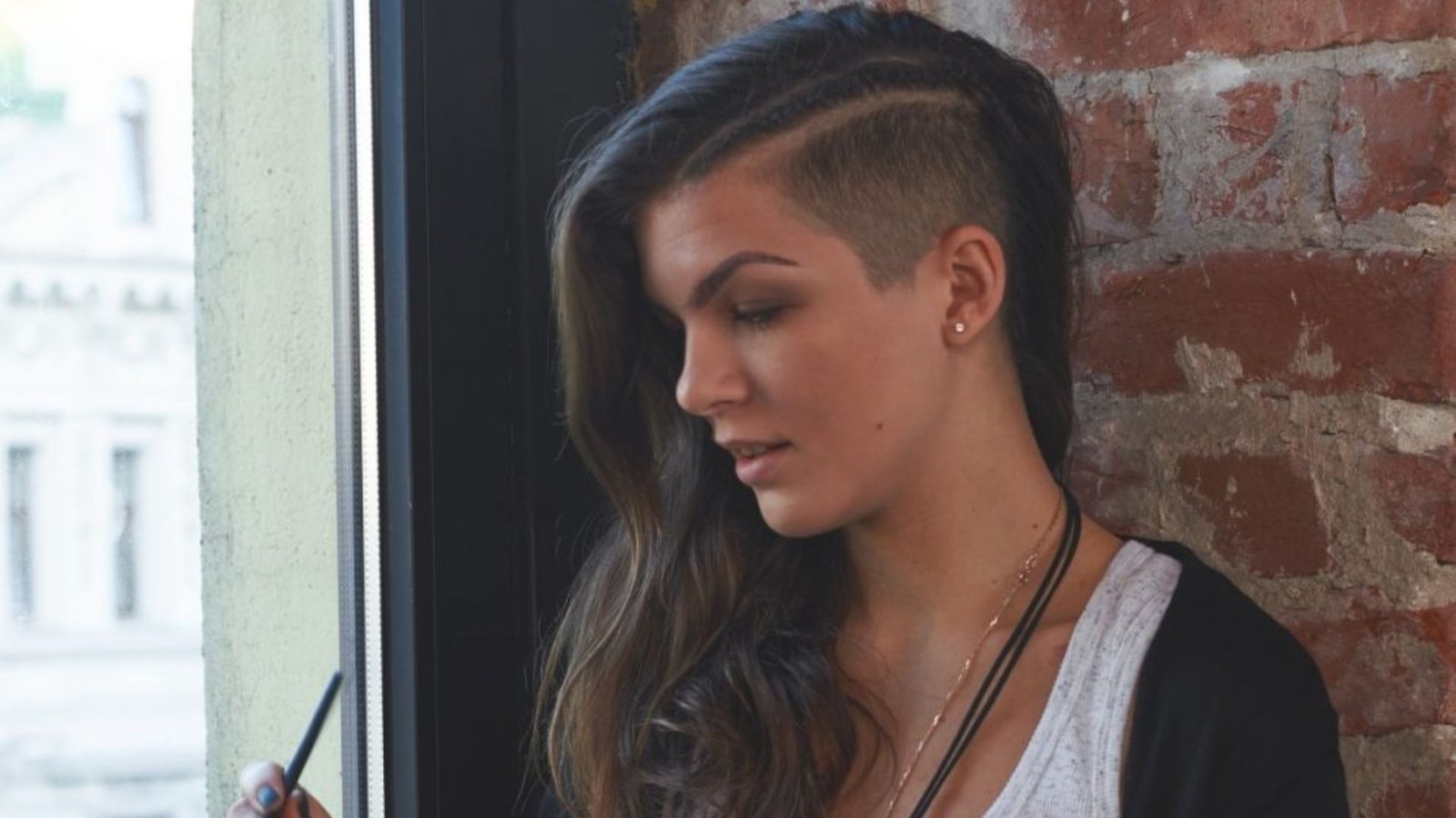 Side profile of a woman with long wavy brown hair and a shaved side undercut.
