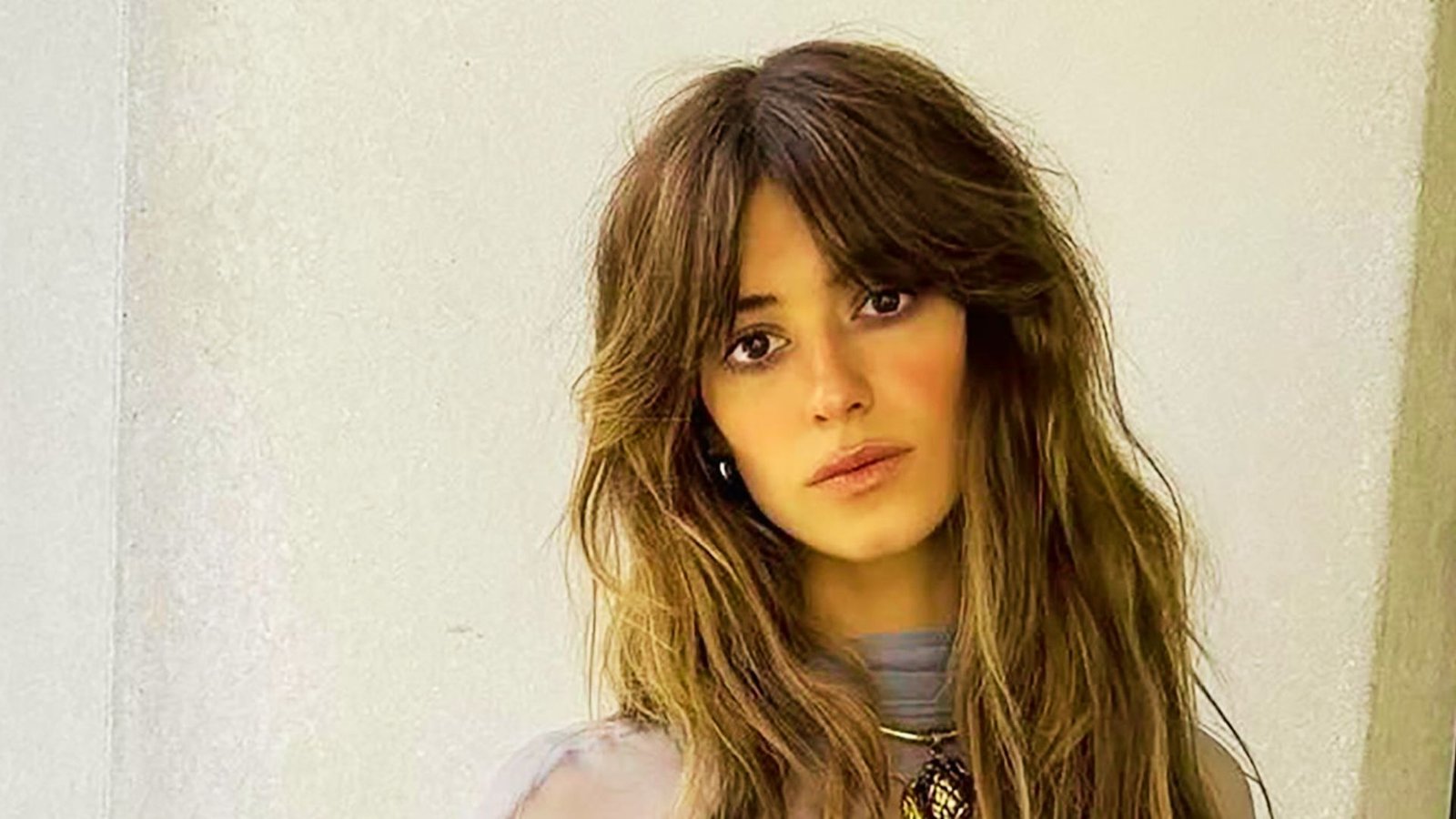 A woman with long, wavy hair styled in thick curtain bangs, showcasing a layered haircut.
