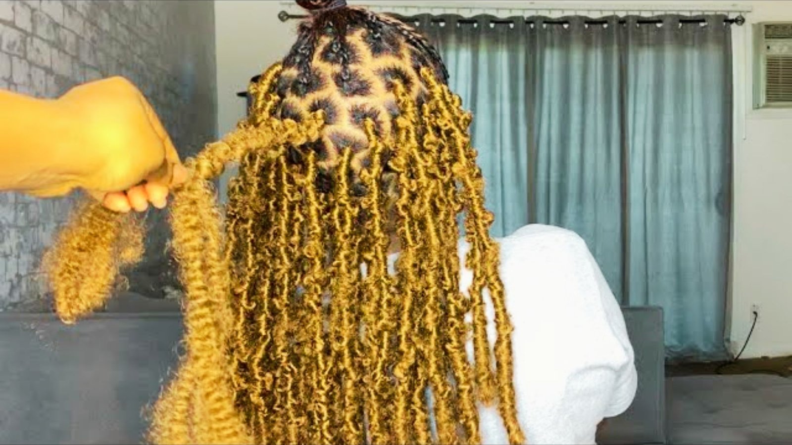 A woman with long black hair brushes her hair, showcasing a Messy Distressed Faux Locs