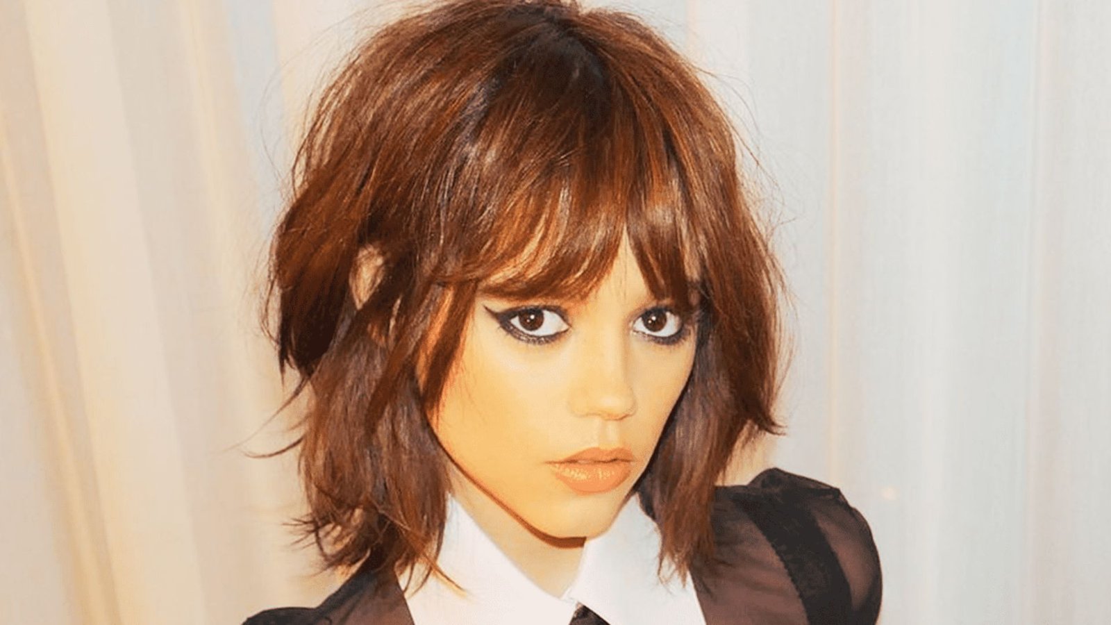 A woman with long hair styled in razor-cut layers and curtain bangs, showcasing her long face.
