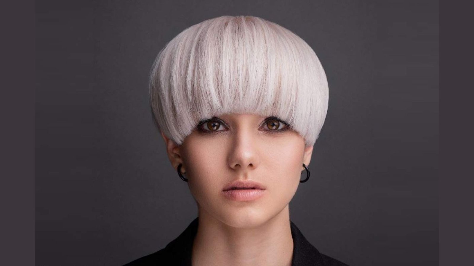 Studio portrait of a woman with a platinum blonde bowl-cut undercut and blunt bangs.