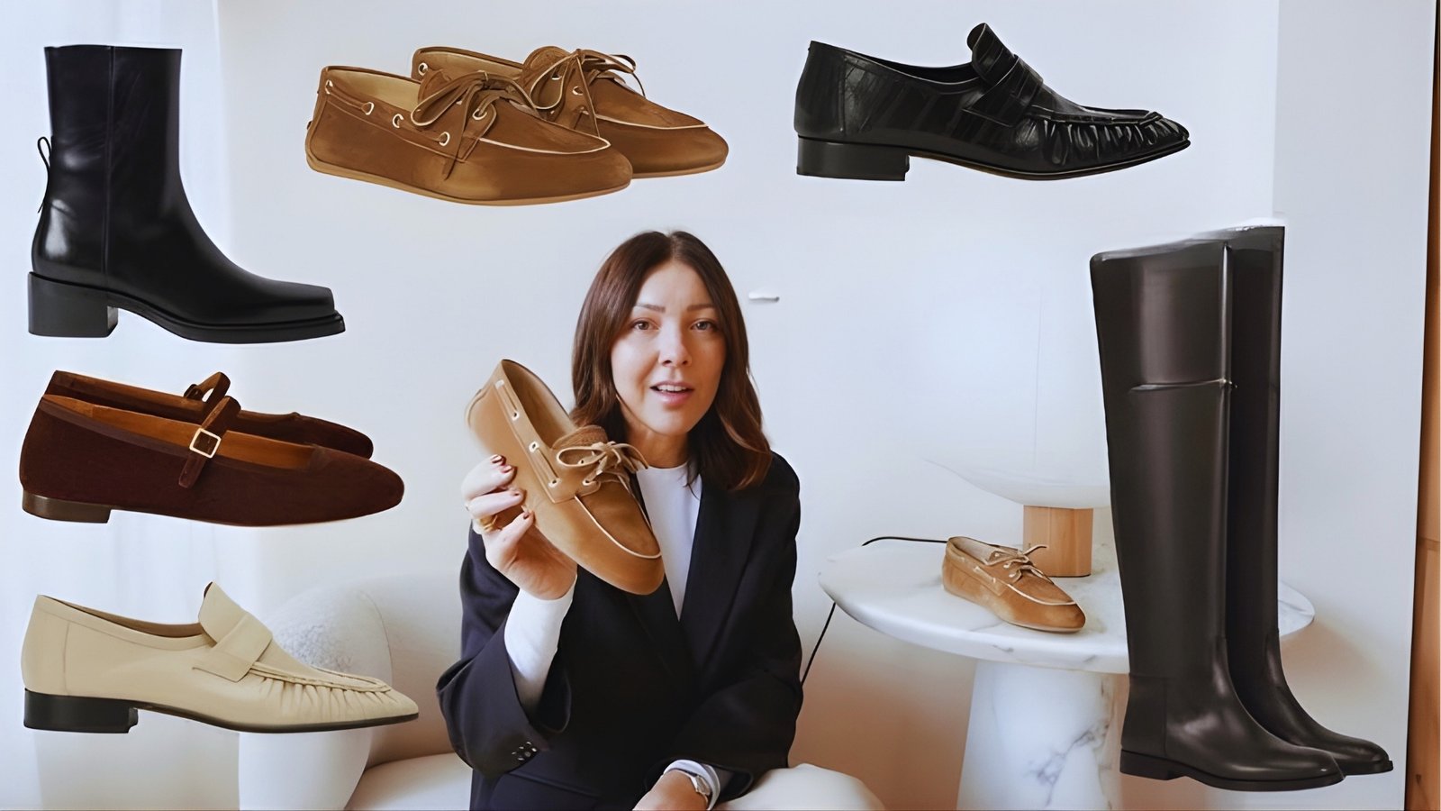 A person in a black suit holds a tan boat shoe in a modern room. Surrounding them are various shoes including boots, loafers, and flats on a plain backdrop.