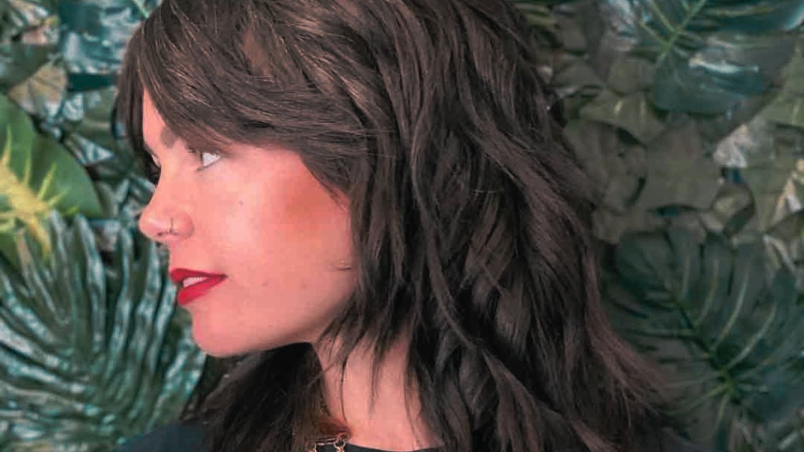 A woman with long brown hair styled in a side-swept bangs mullet and wearing red lipstick.