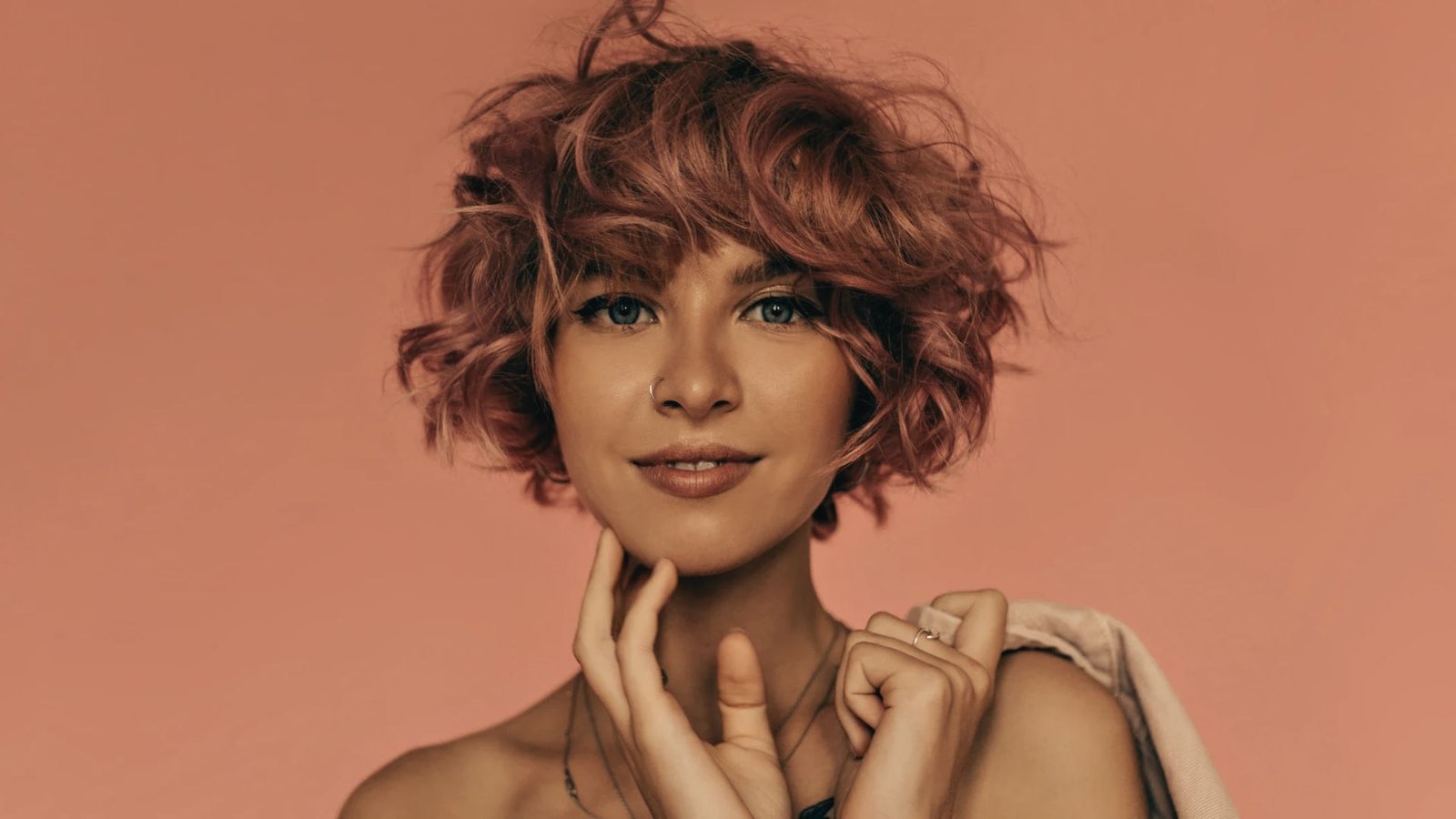 A woman with a curly, choppy pixie cut in pink hair poses confidently for the camera.