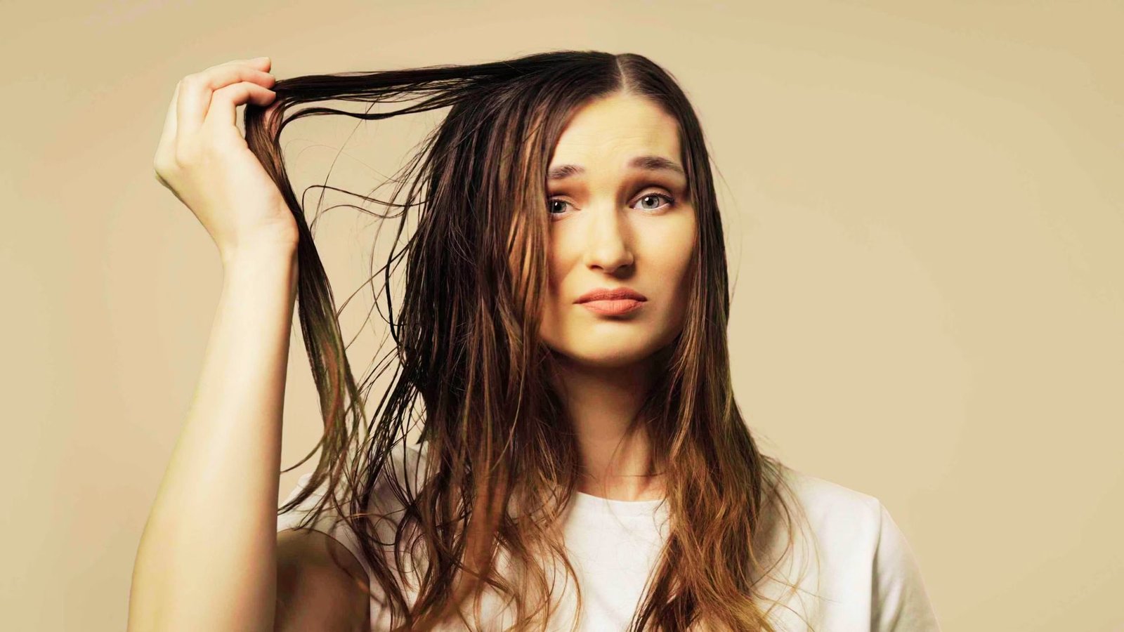 A woman with long hair combs her greasy hair, looking for quick solutions to freshen it up before heading out.