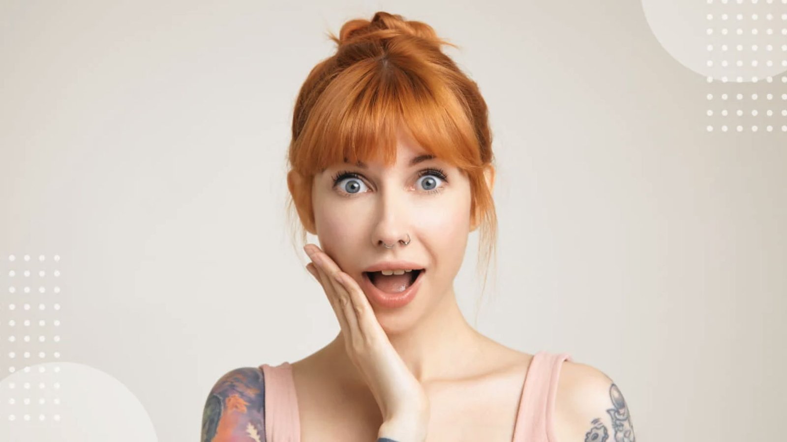 A surprised woman with a messy bun and sleek bangs shows her tattooed arm, expressing astonishment.