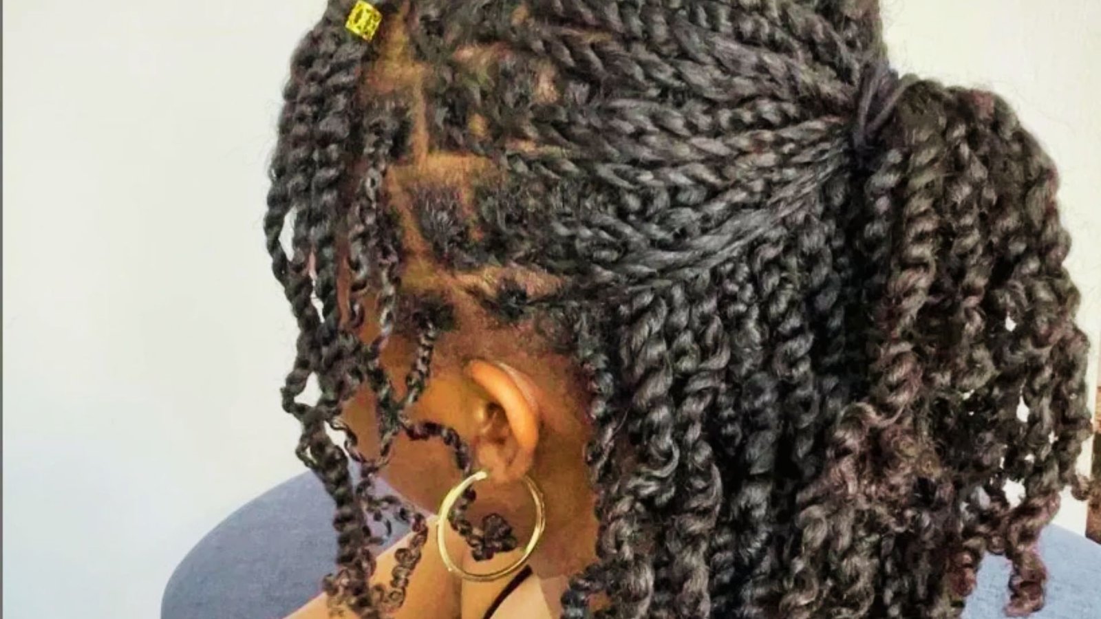 A woman with long braids styled in Senegalese twists, demonstrating a step in a hair curling tutorial.