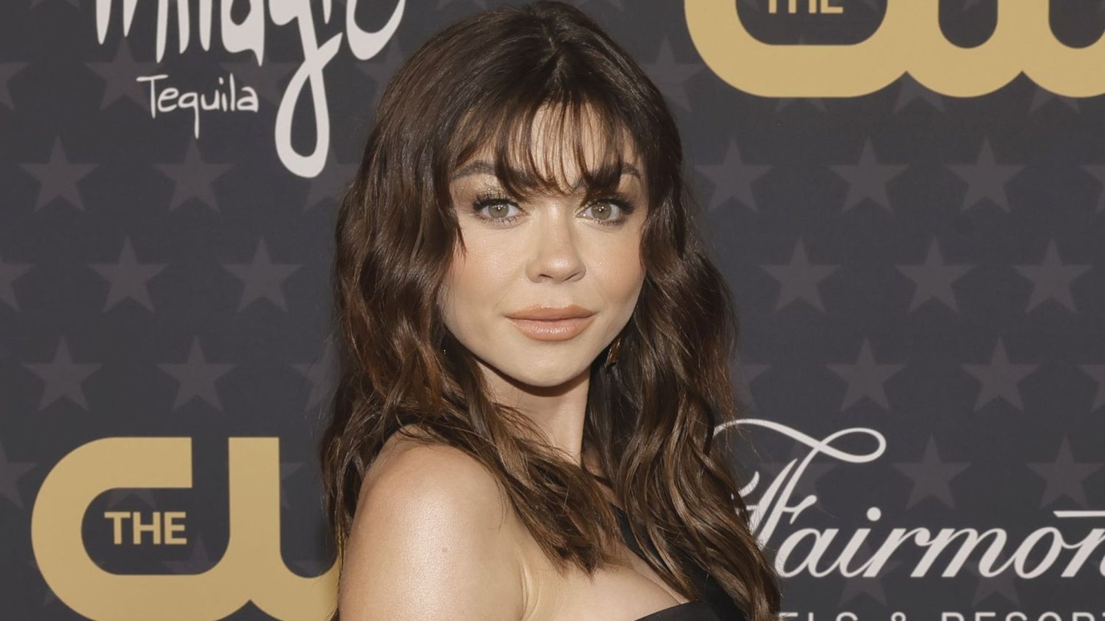 Woman at an event with long wavy hair and soft, eyebrow-skimming bangs. The fringe is slightly parted in the center with blended side pieces.