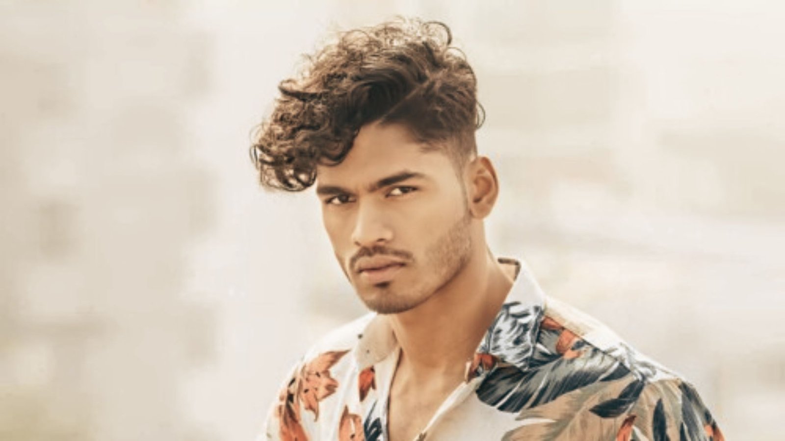 A man with curly hair wearing a floral shirt, showcasing a disconnected undercut fade hairstyle.