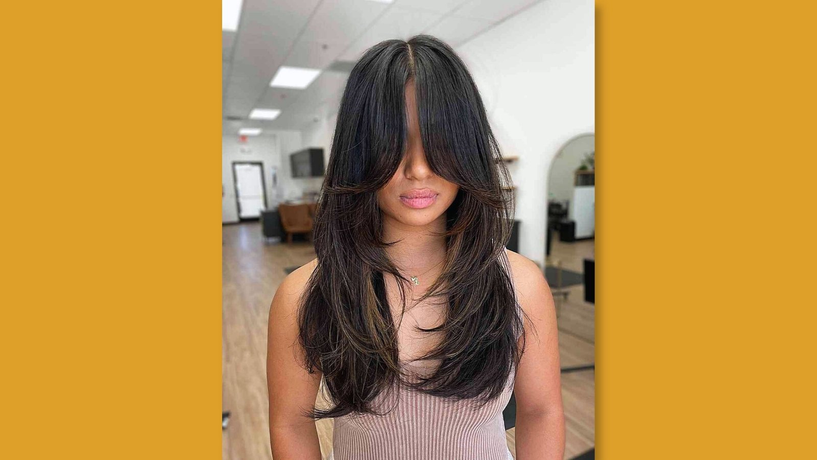 Low maintenance layered long haircut with heavy curtain bangs and face-framing layers on dark brown hair with subtle highlights for round face 
