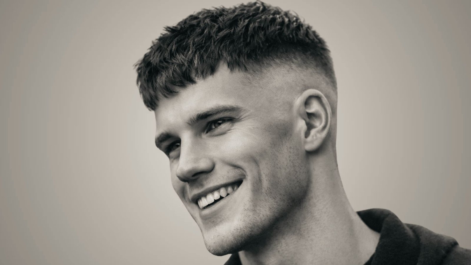 A man with a French crop disconnected undercut fade smiles confidently at the camera.