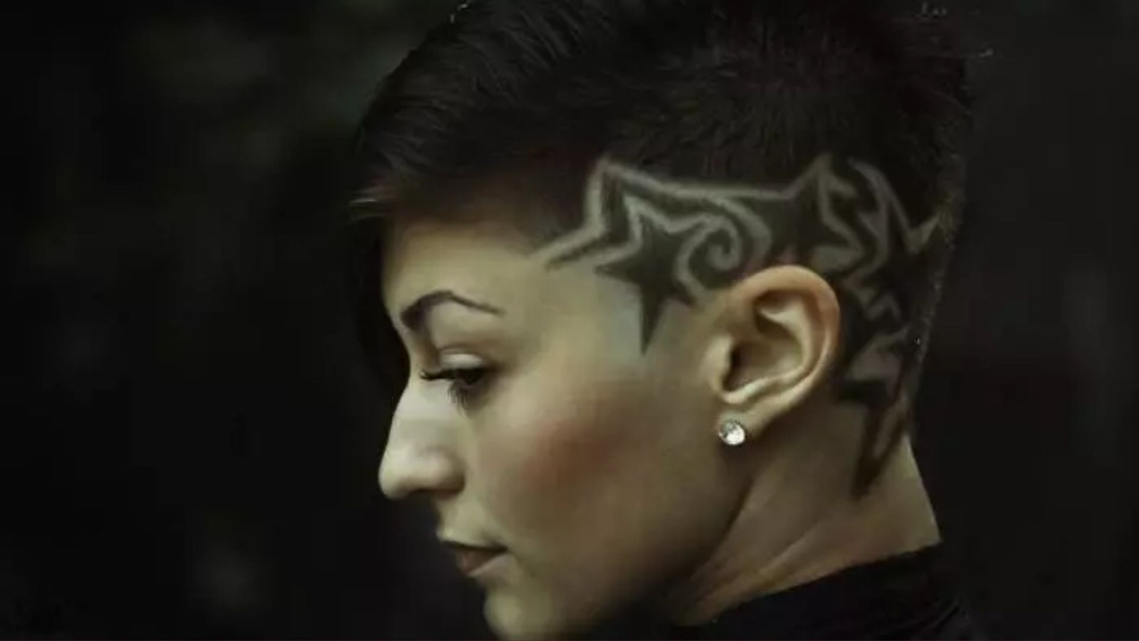 Side profile of a woman with short dark hair and intricate star and tribal designs shaved into the side undercut.