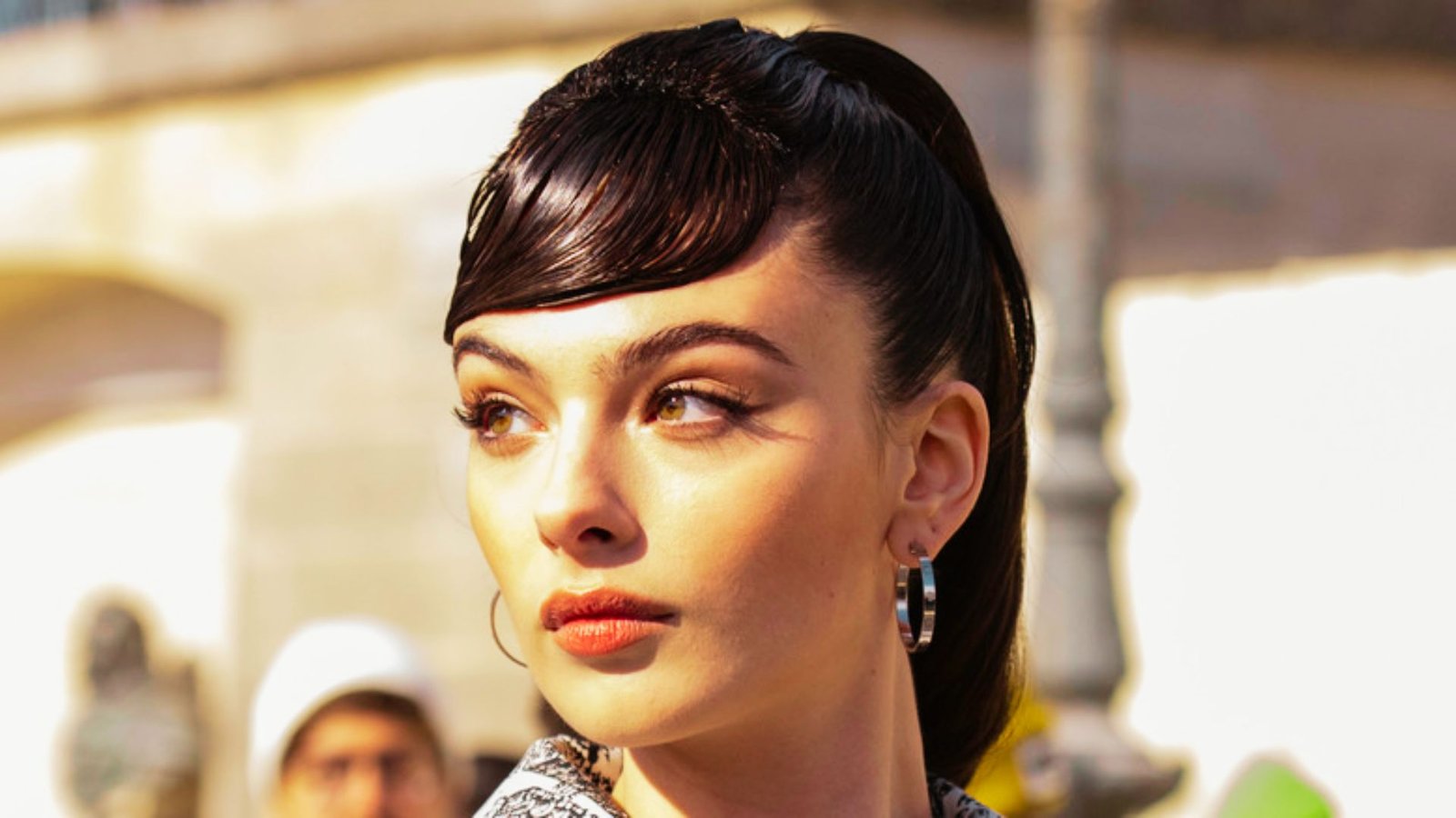 A woman with a ponytail and earrings, showcasing deep side-part bangs, highlighting her face shape.

