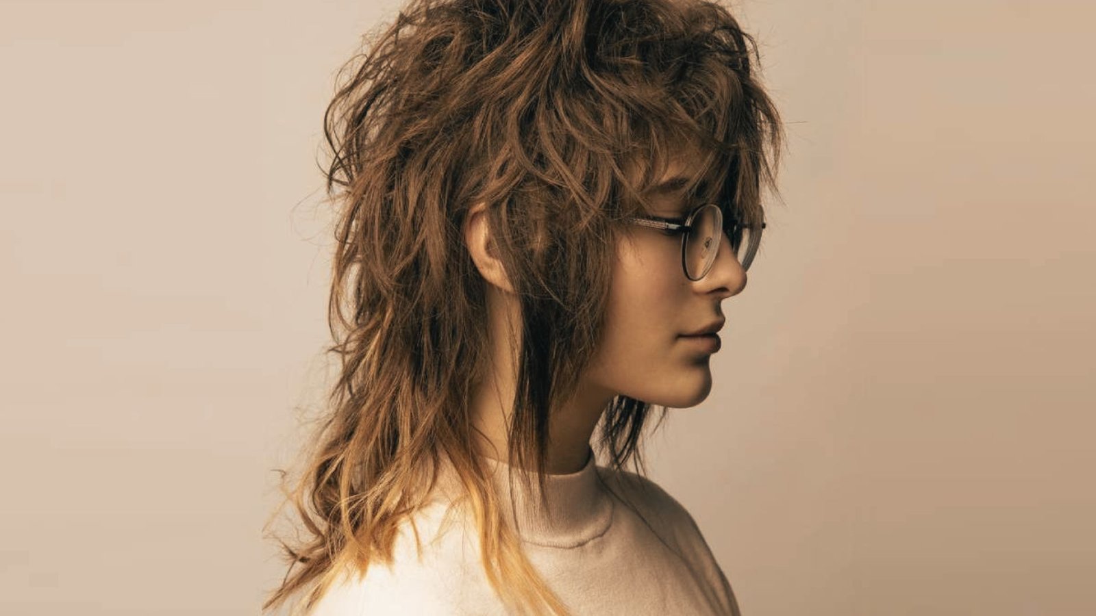 A woman with long hair styled in a feathered mullet, wearing glasses.