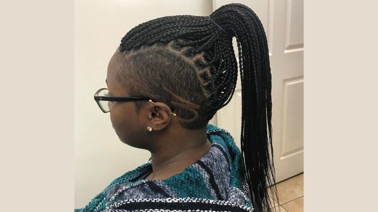 Side profile of a woman with box braids in a high ponytail and curved line designs in the side undercut.