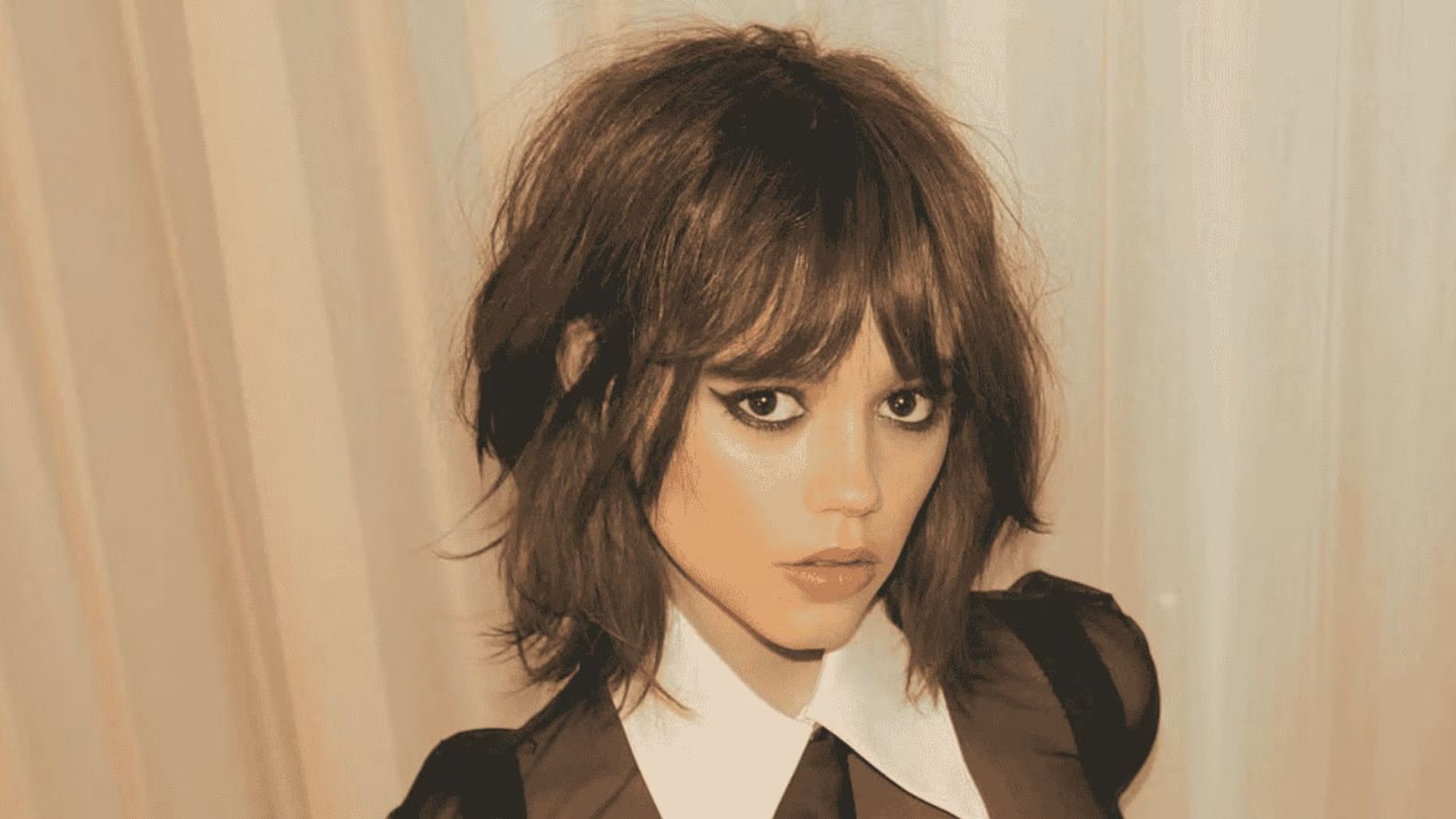 A woman with a wolf cut mullet hairstyle, wearing a black and white shirt and tie.
