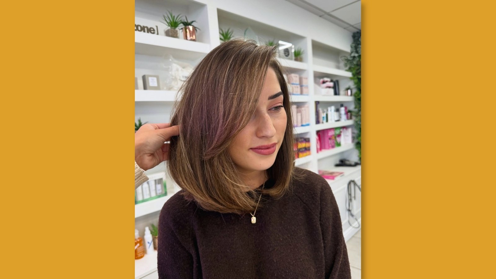 Brunette shoulder length haircut with long side-swept bangs and subtle layers shown in salon with product shelves
