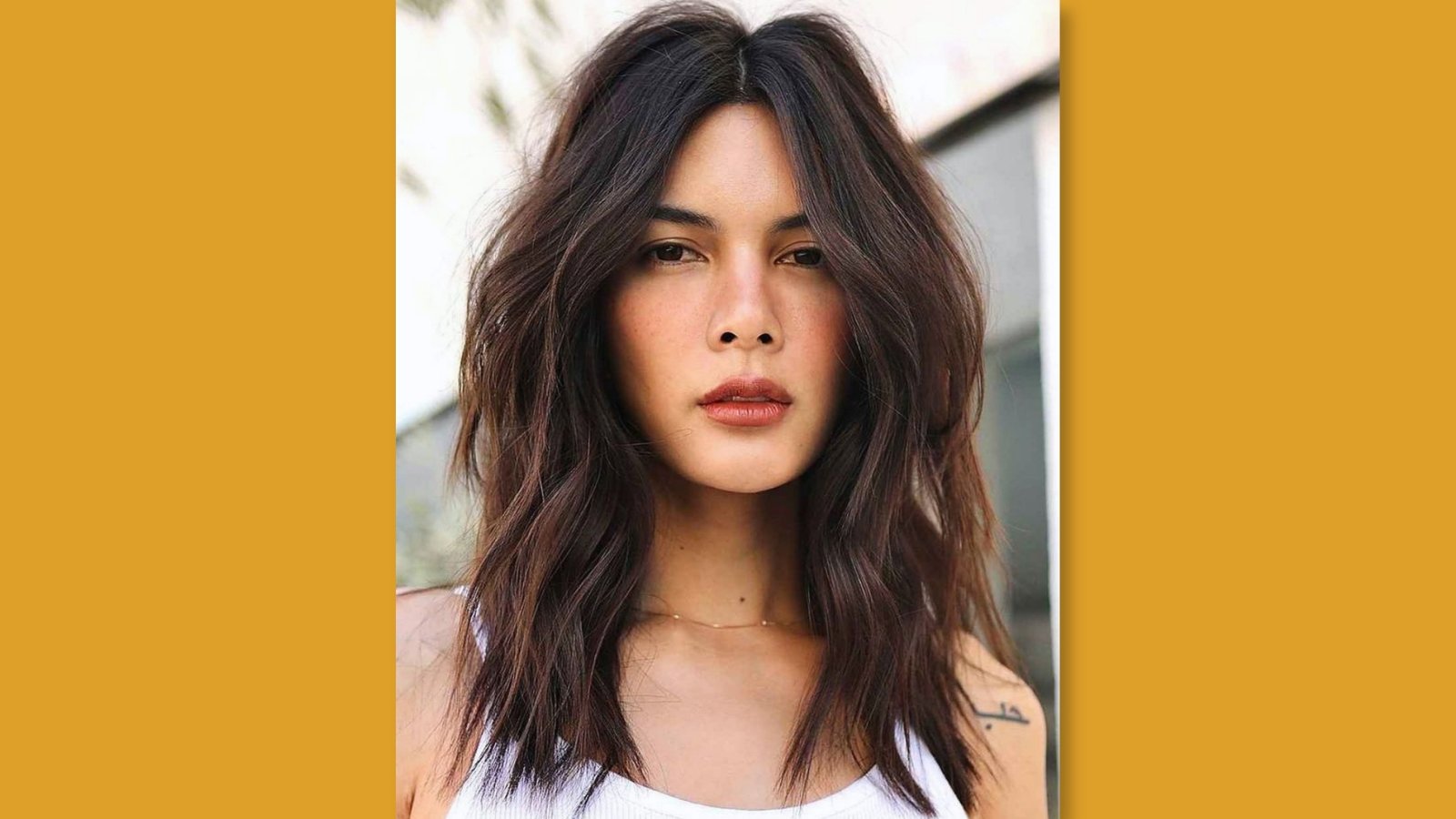 Low maintenance layered medium length haircut with center part and tousled face-framing waves on dark brunette hair for round face 
