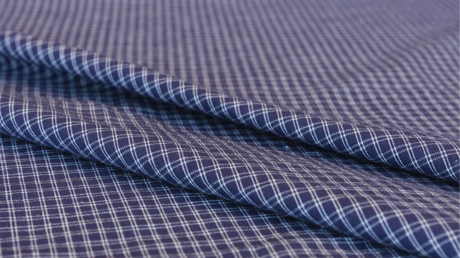 Blue fabric with a white plaid pattern is neatly folded. The texture appears smooth and soft, giving a sense of quality and sophistication.