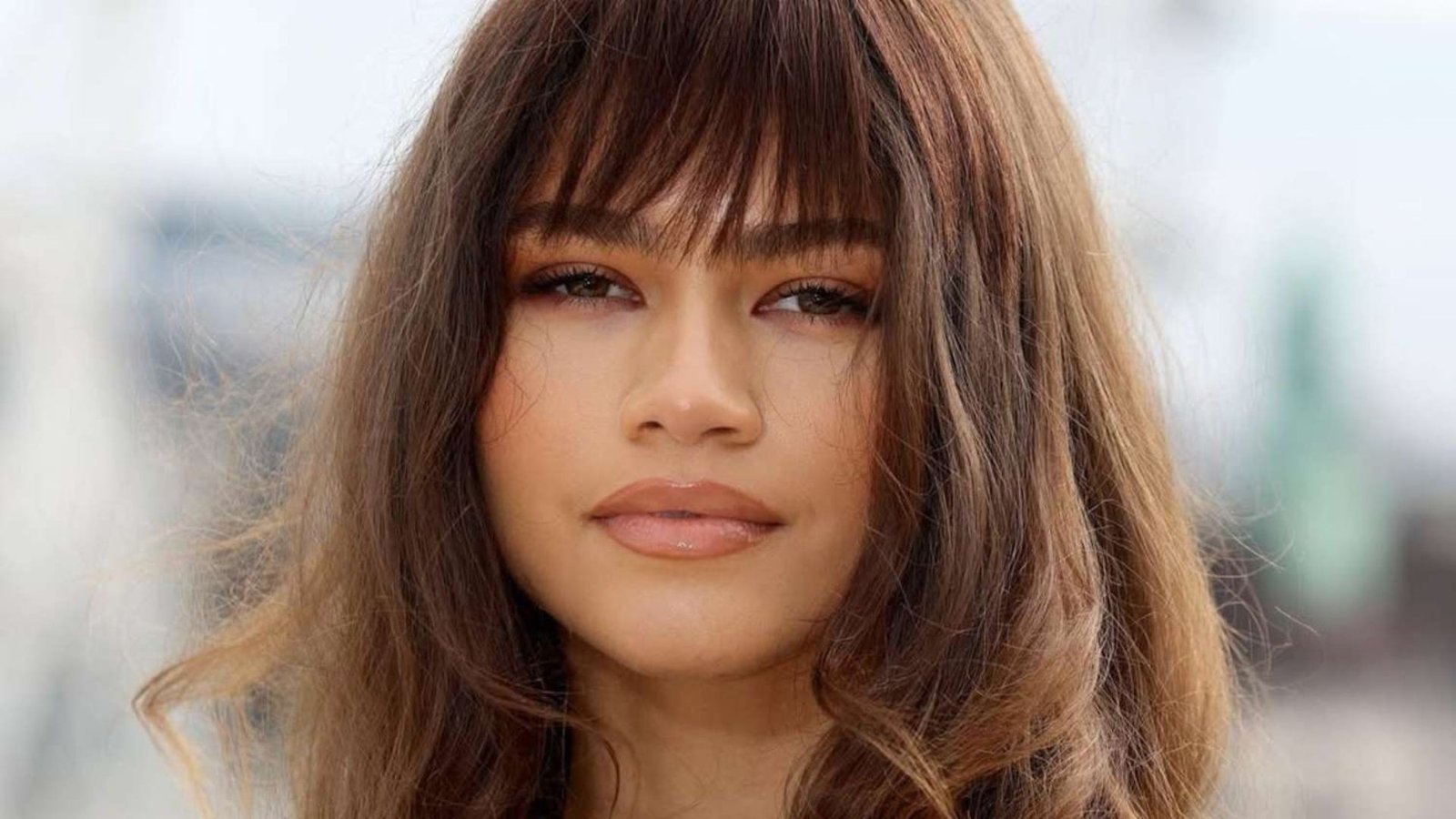 Close-up of a woman with long, straight hair and wispy, brow-grazing bangs. The fringe is light and feathery with face-framing layers.
