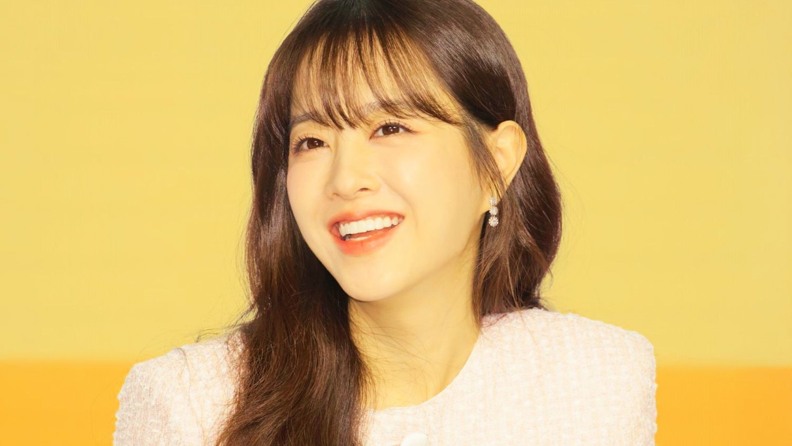 A woman with long, layered hair and curtain bangs, showcasing a Korean-inspired hairstyle.
