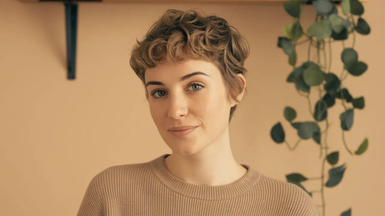 A woman in a brown sweater with short hair, showcasing her low maintenance curly pixie cut hair care routine.