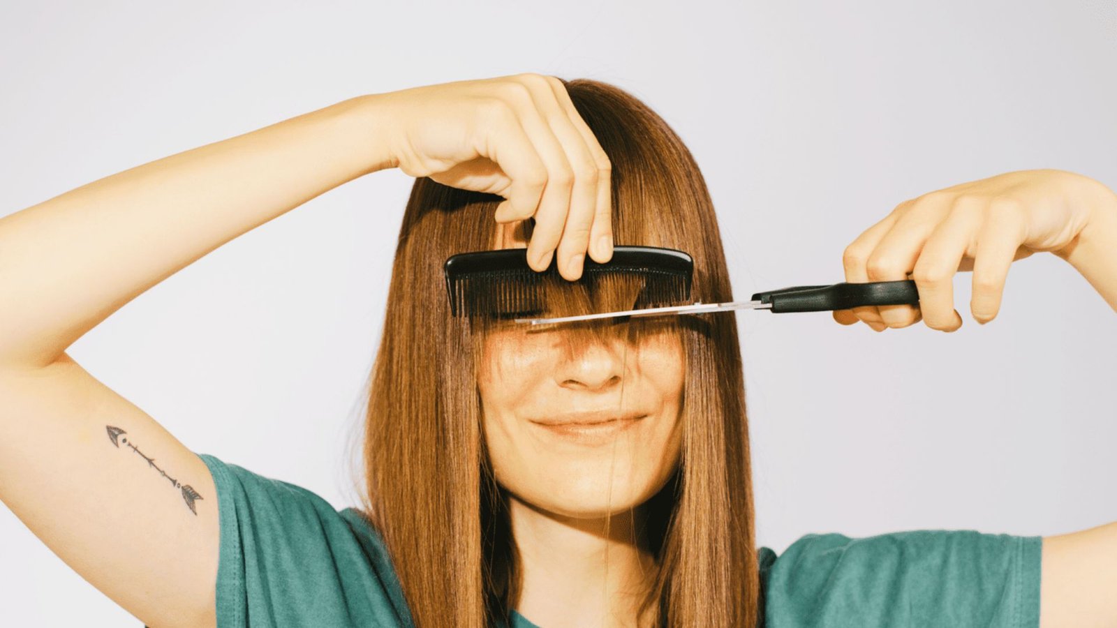 A woman cuts her hair with scissors, preparing to style Bardot bangs at home.
