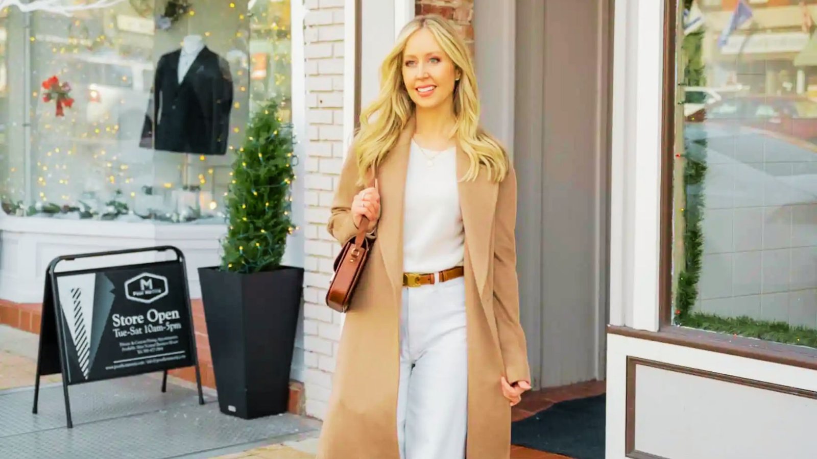 A blonde woman wearing white pants and a camel coat, embodying a stylish athleisure look suitable for busy moms.