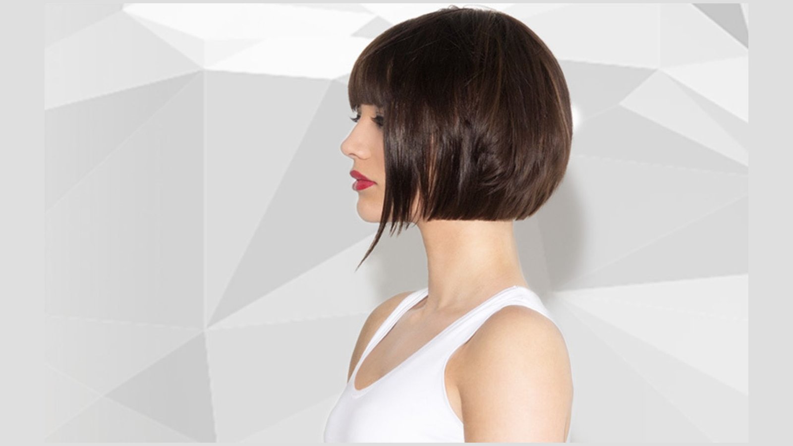 Side profile of a woman with a sleek dark brown bob and blunt bangs wearing a white tank top.
