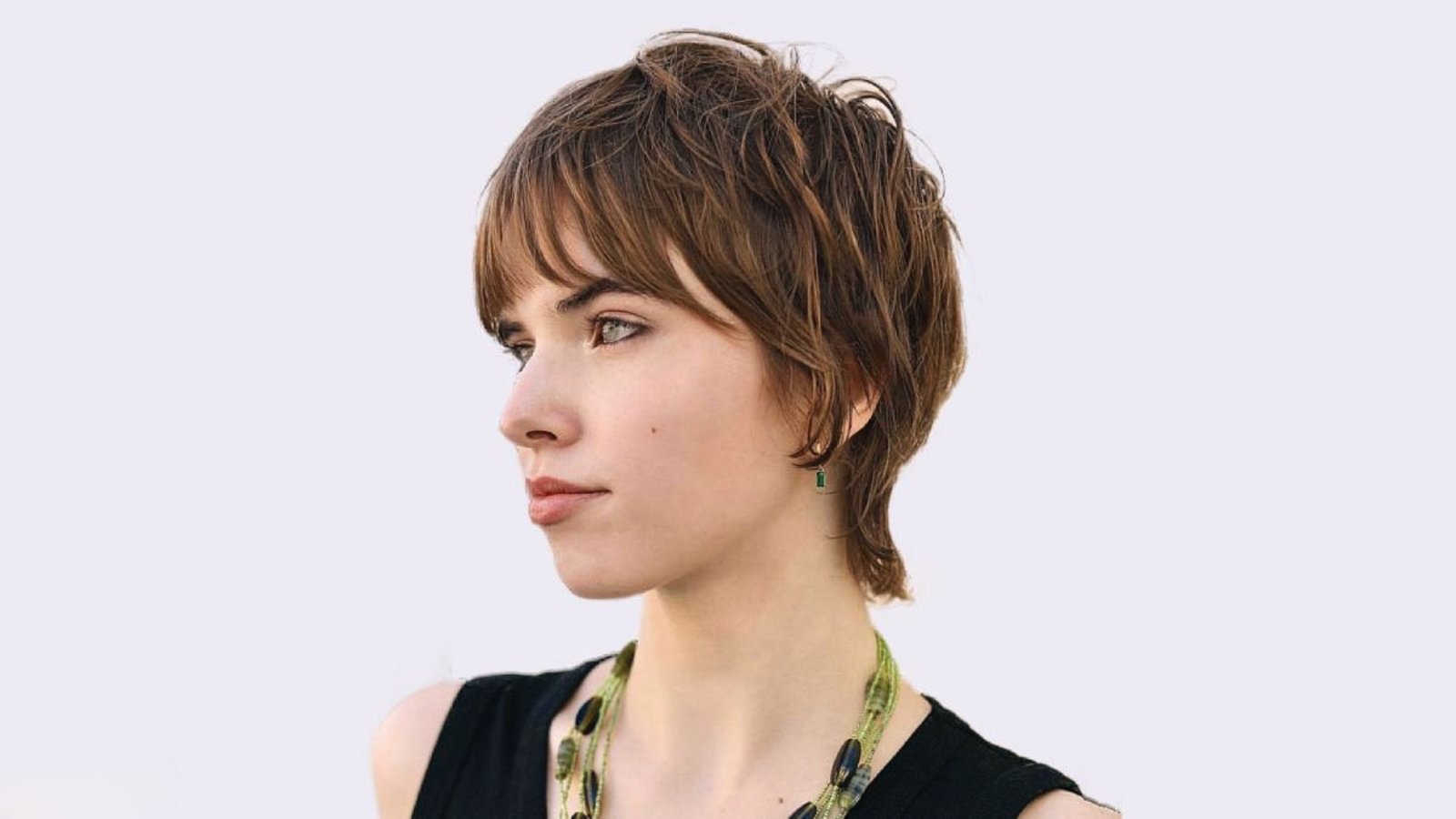 A woman with a full fringe mullet haircut wearing a necklace, looking confidently at the camera.