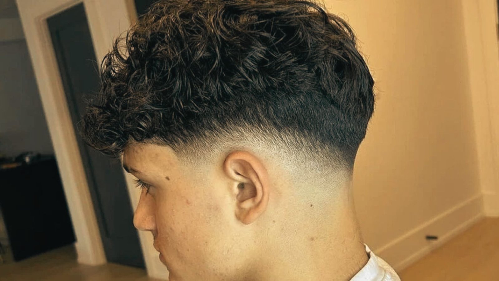 A man with curly hair styled in a layered flow disconnected undercut fade.