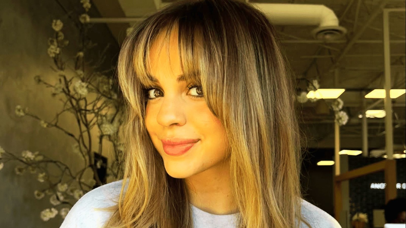 A woman with long, thick hair styled in layers, featuring prominent curtain bangs framing her face.