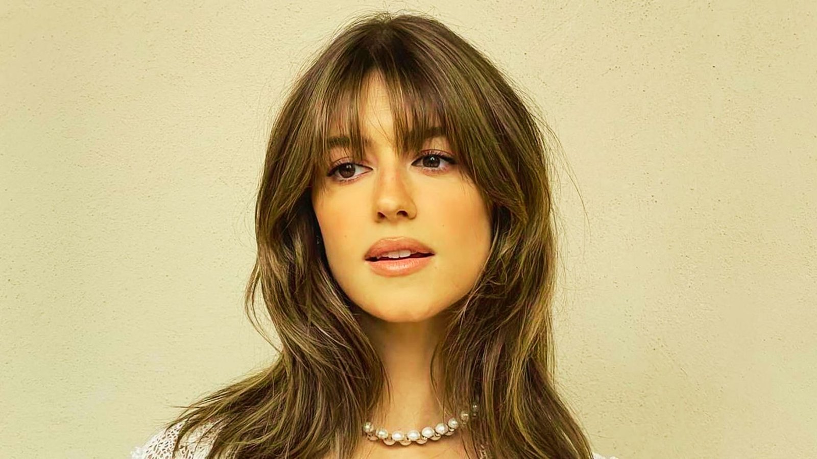 A woman with long hair wearing a white top, illustrating tips on selecting bangs for various face shapes.
