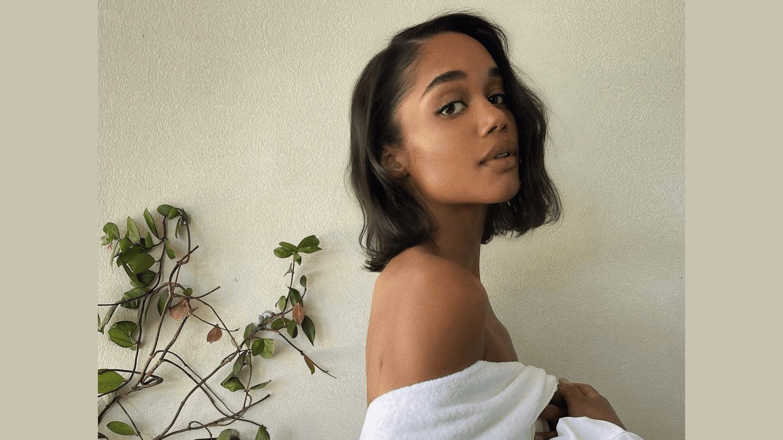 Woman with shoulder-length dark wavy hair in a white off-shoulder top looking over her shoulder.