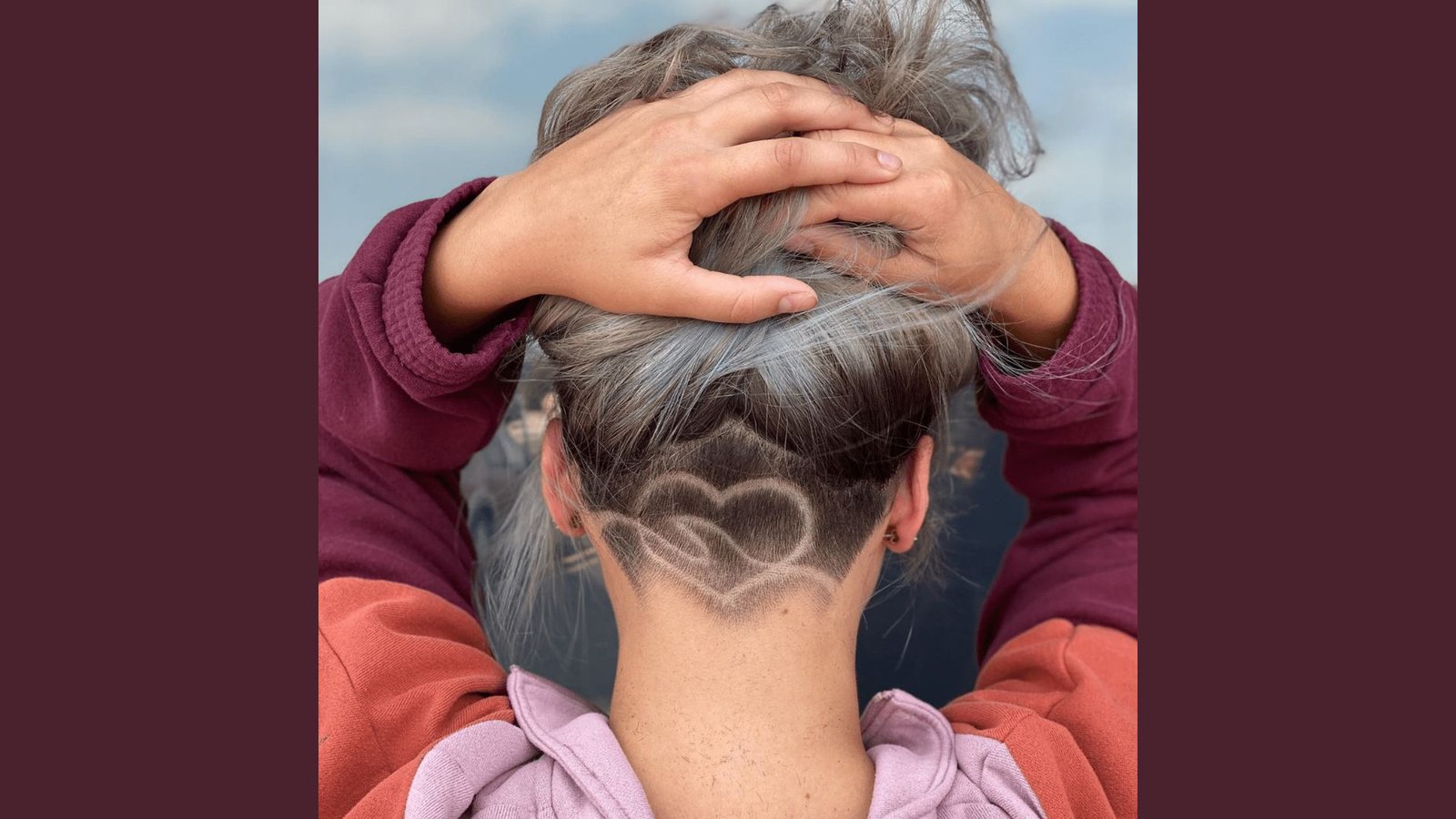 Back view of a woman with silver-gray hair lifted to reveal a double heart design shaved into the nape undercut.