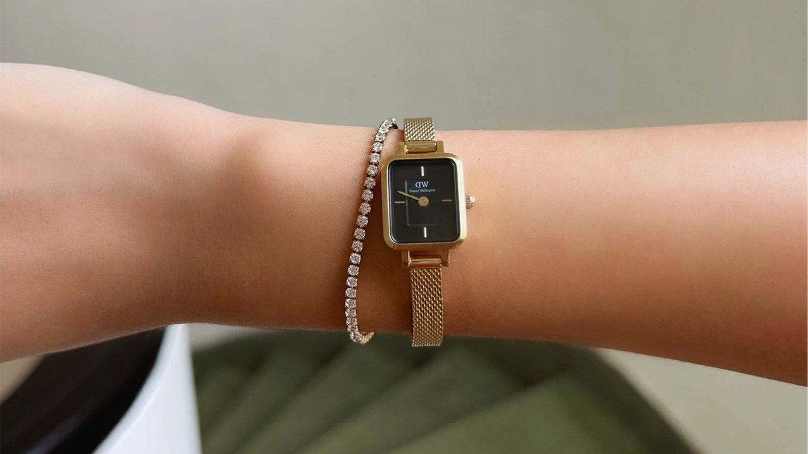 A wrist adorned with a sleek gold watch featuring a black square face on a mesh band, paired with a sparkling diamond bracelet, exudes elegance.