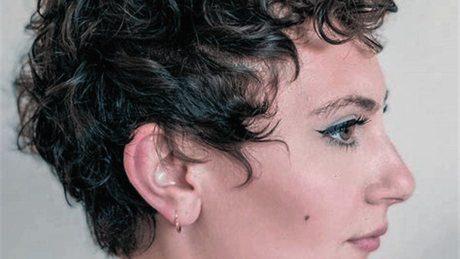A woman with short curly hair gazes to the side, showcasing a stylish low-maintenance pixie cut.