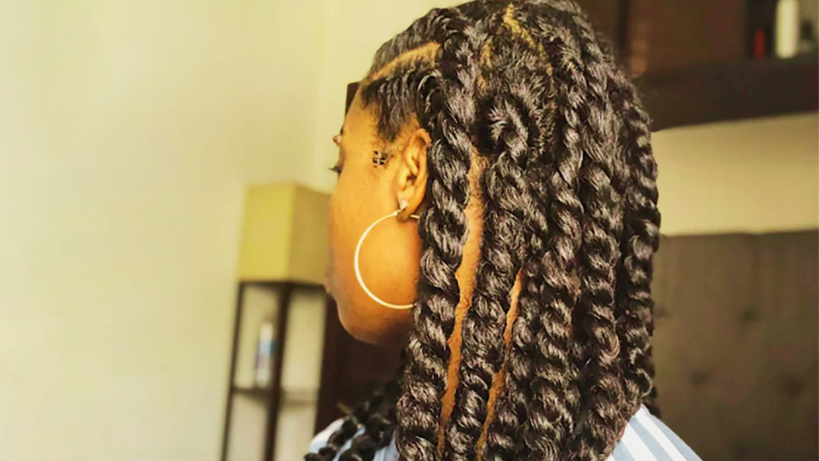A woman with long black hair styled in Senegalese twists and curls, demonstrating a hair tutorial.