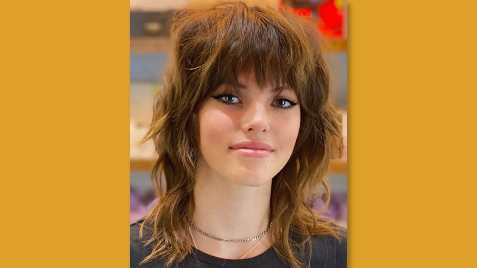 Low maintenance medium length shag haircut with full textured bangs and choppy layers on warm brown hair for round face
