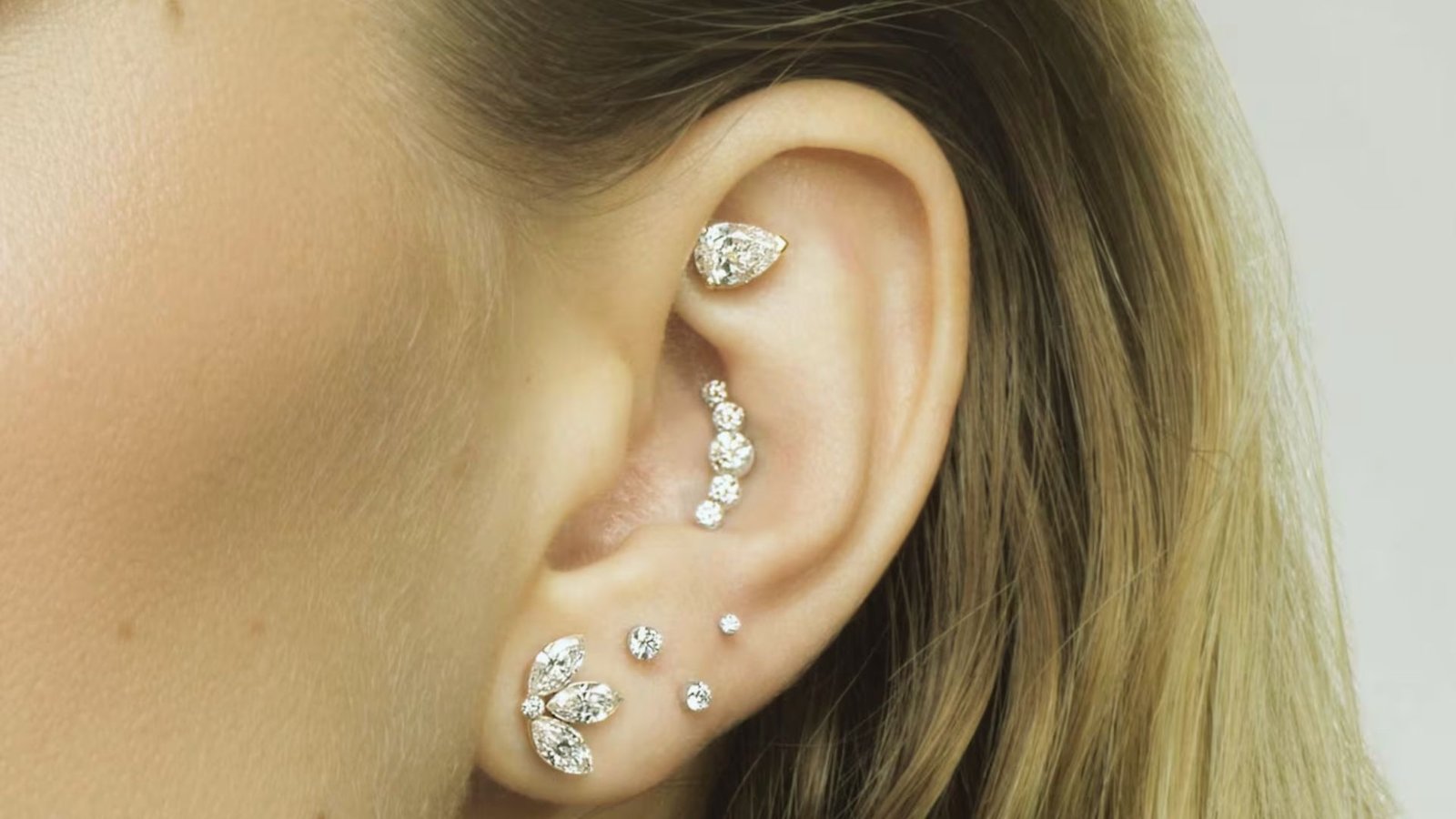 Close-up of an ear adorned with multiple diamond earrings of various shapes and sizes, showcasing an elegant and luxurious style.