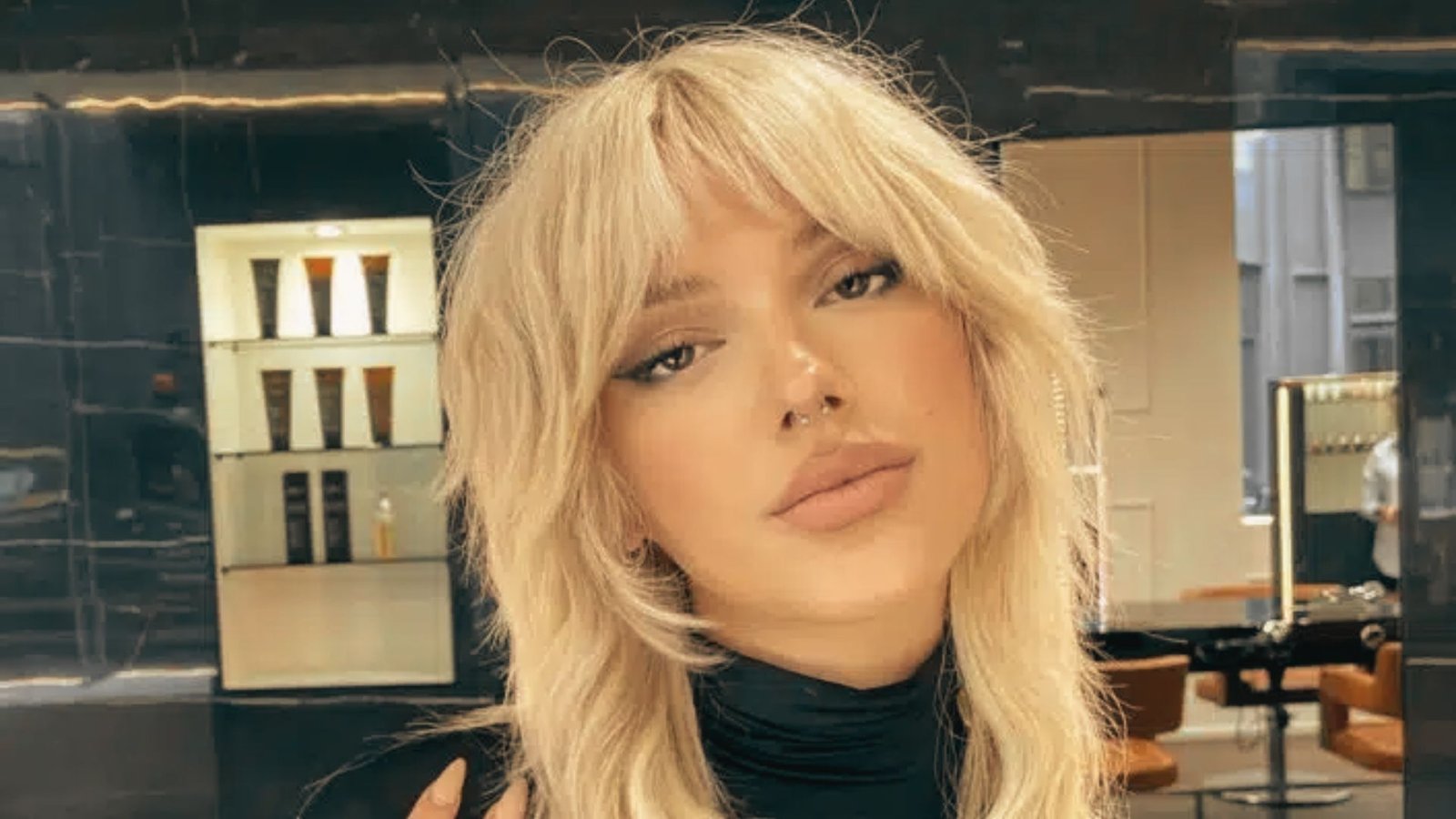 A woman with long, voluminous blonde hair styled in a layered mullet poses for a photo.