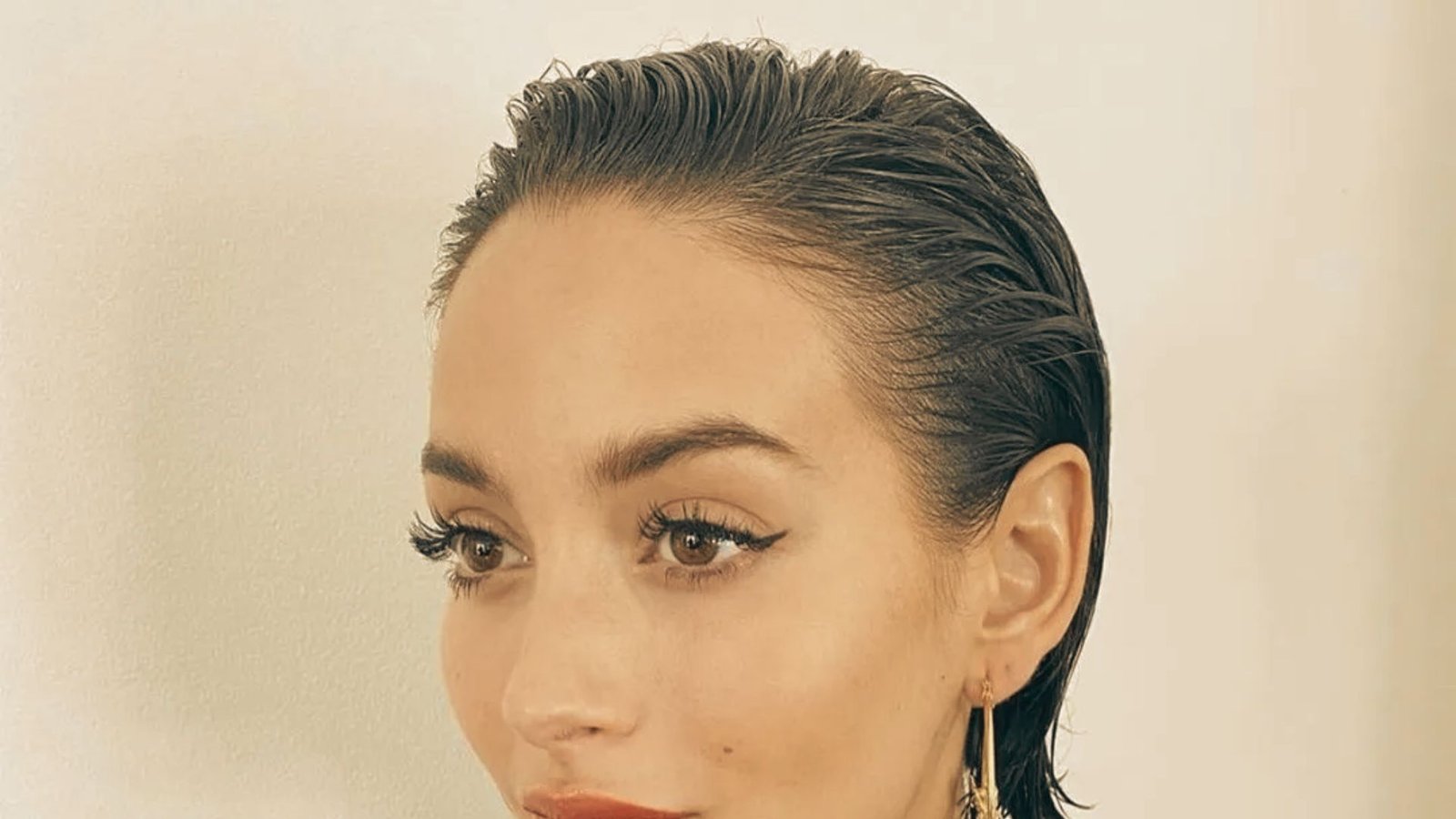 A woman with pixie cut hair and earrings, preparing to style her hair while it is wet or damp.