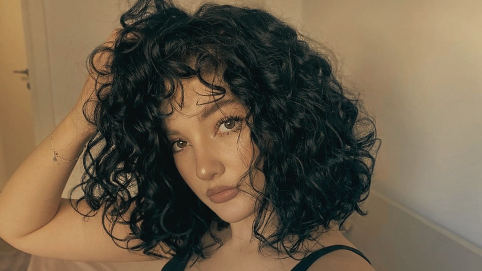 A woman with curly hair smiling, highlighting her trendy curtain bangs.