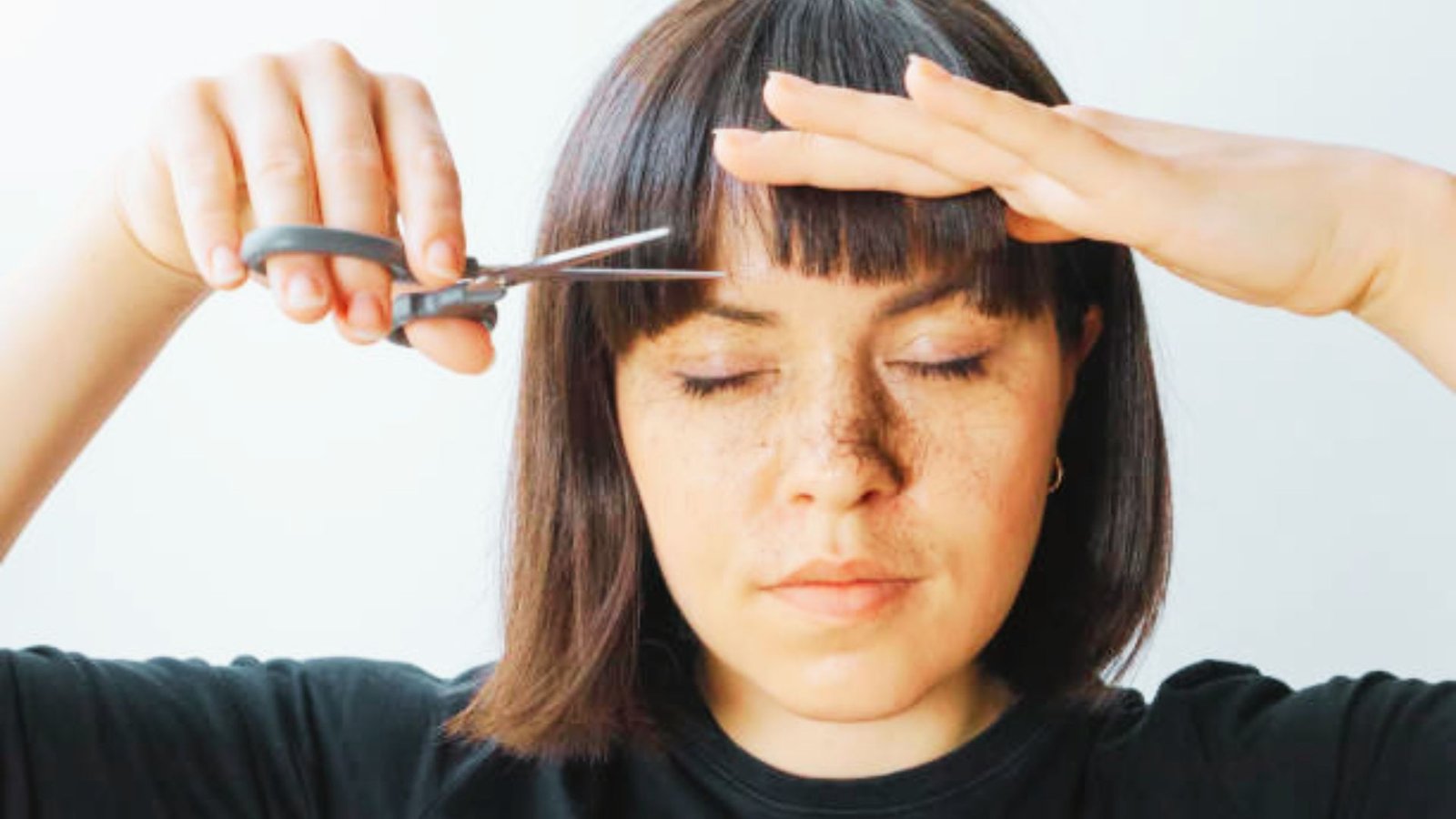 A woman cutting her hair with scissors
