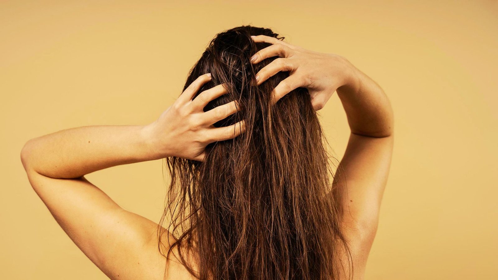 A woman with long hair is gently combing her hair, focusing on maintaining its smoothness and shine.
