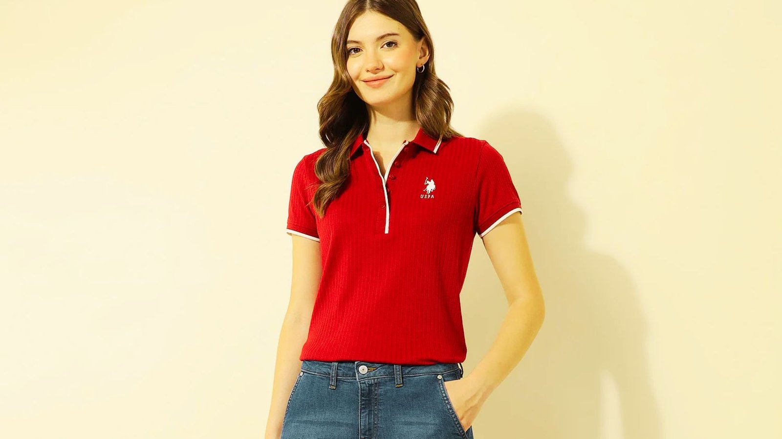 A woman in a fitted polo shirt and bootcut jeans stands confidently embodying a preppy 2000s style.